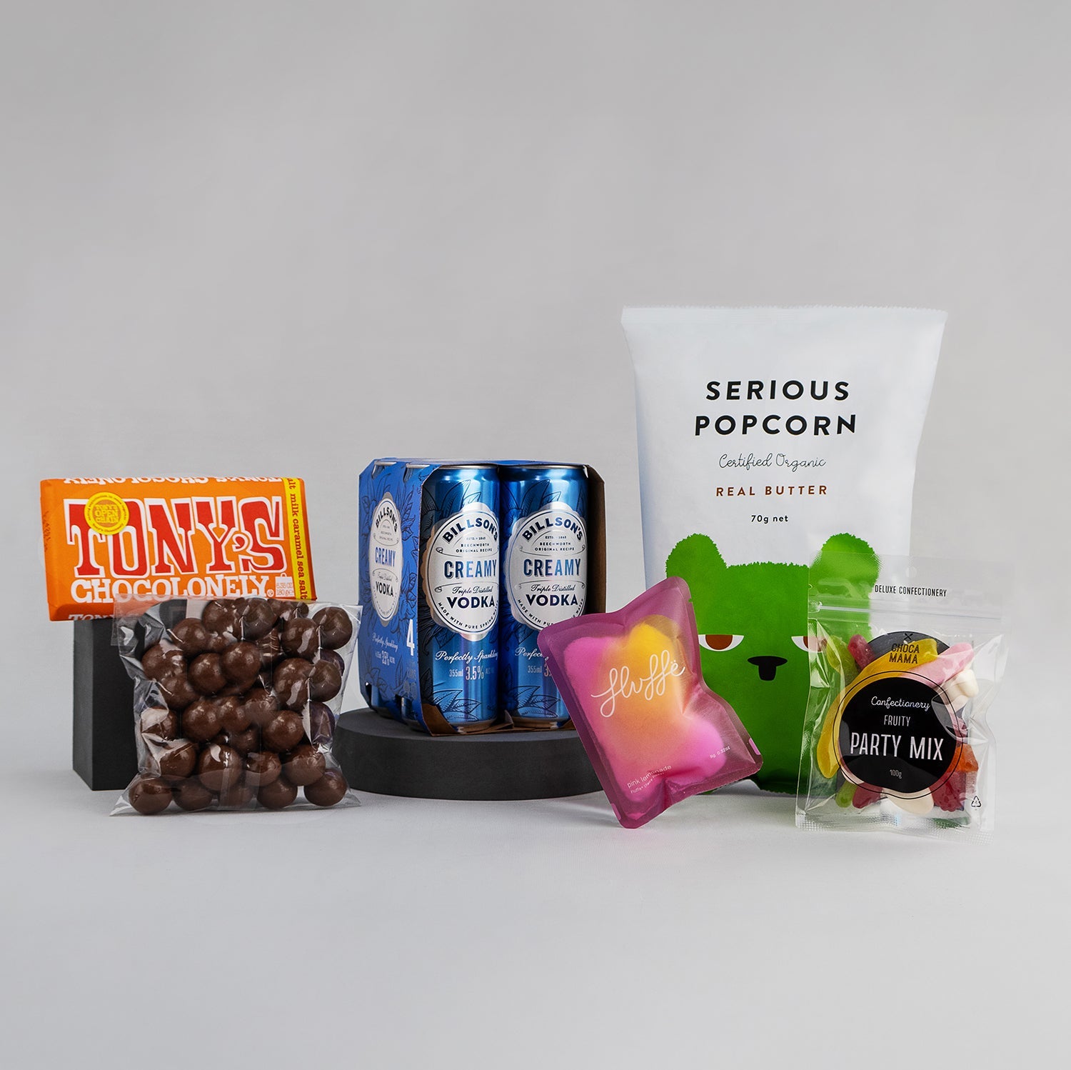 Gift hamper featuring three blue cans of Billson's vodka, a bag of Serious Popcorn, chocolate-covered treats, a pink.