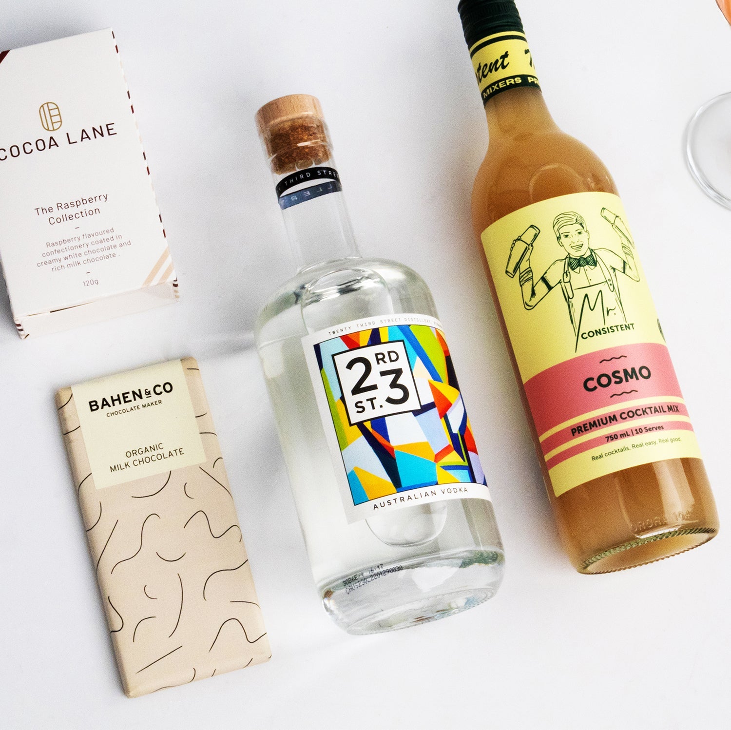 Cosmo Hamper with colorful 273 gin bottle, creamy Cosmo cocktail mixer, and two artisanal chocolate bars on white background.