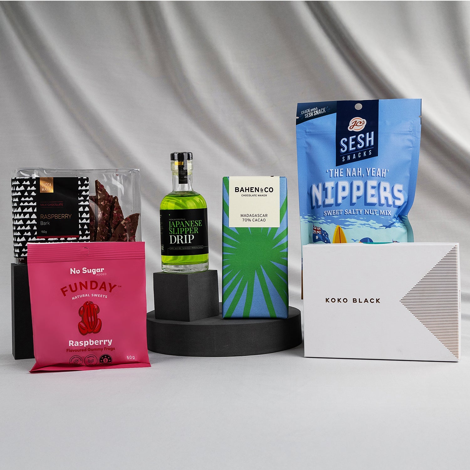 Assortment of Japanese-themed gift items including green bottle, blue snack bag, pink raspberry pouch, white chocolate box,.