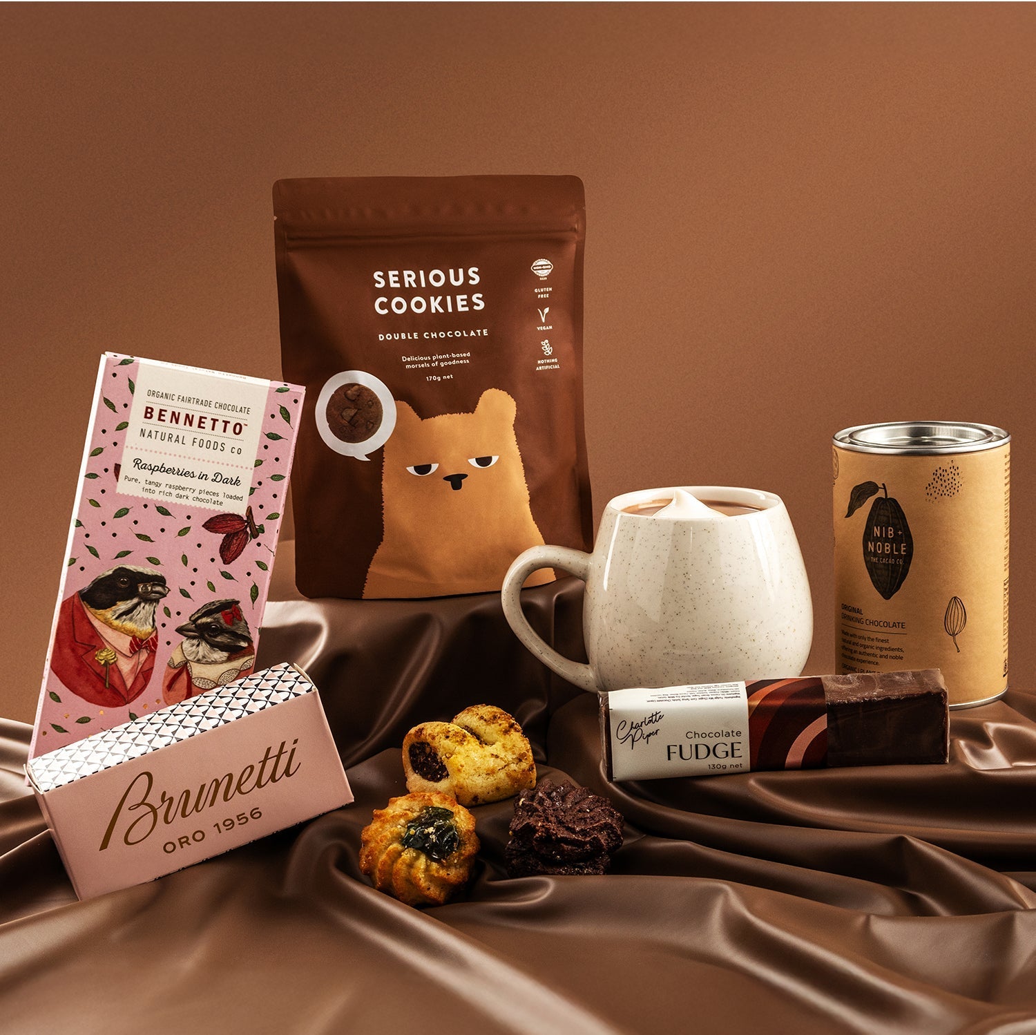 Chocolate Lovers Delight Hamper with Brunetti cookies, Serious Cookies pouch, white mug, fudge bar, and pastries on brown.
