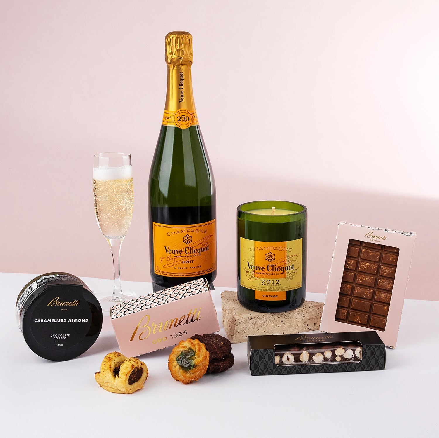 Bottle of Veuve Clicquot champagne with flute, green scented candle, assorted chocolates, candied nuts, and gourmet pastries .