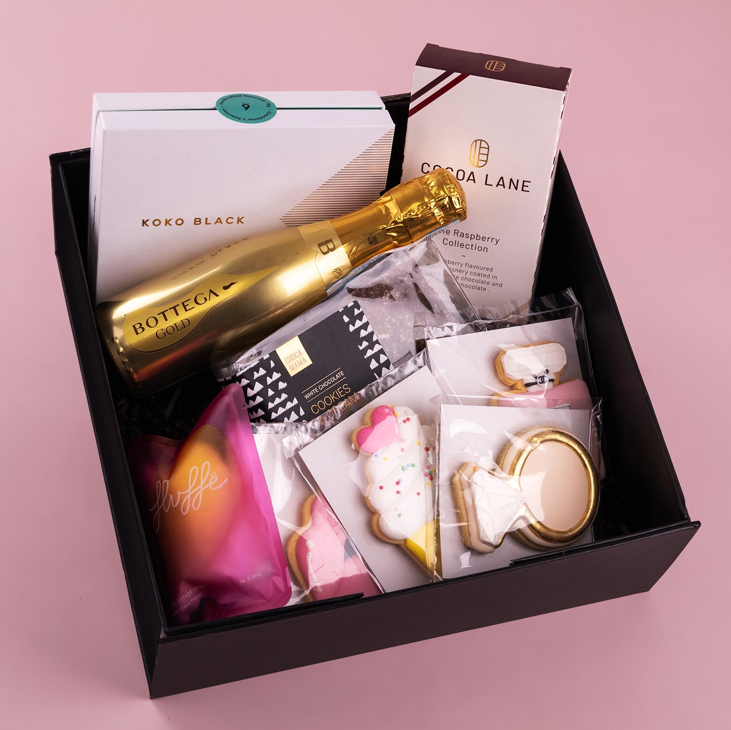 Black gift box with gold Bottega sparkling wine, Koko Black chocolate box, Lola Lane treats, and assorted decorated cookies.
