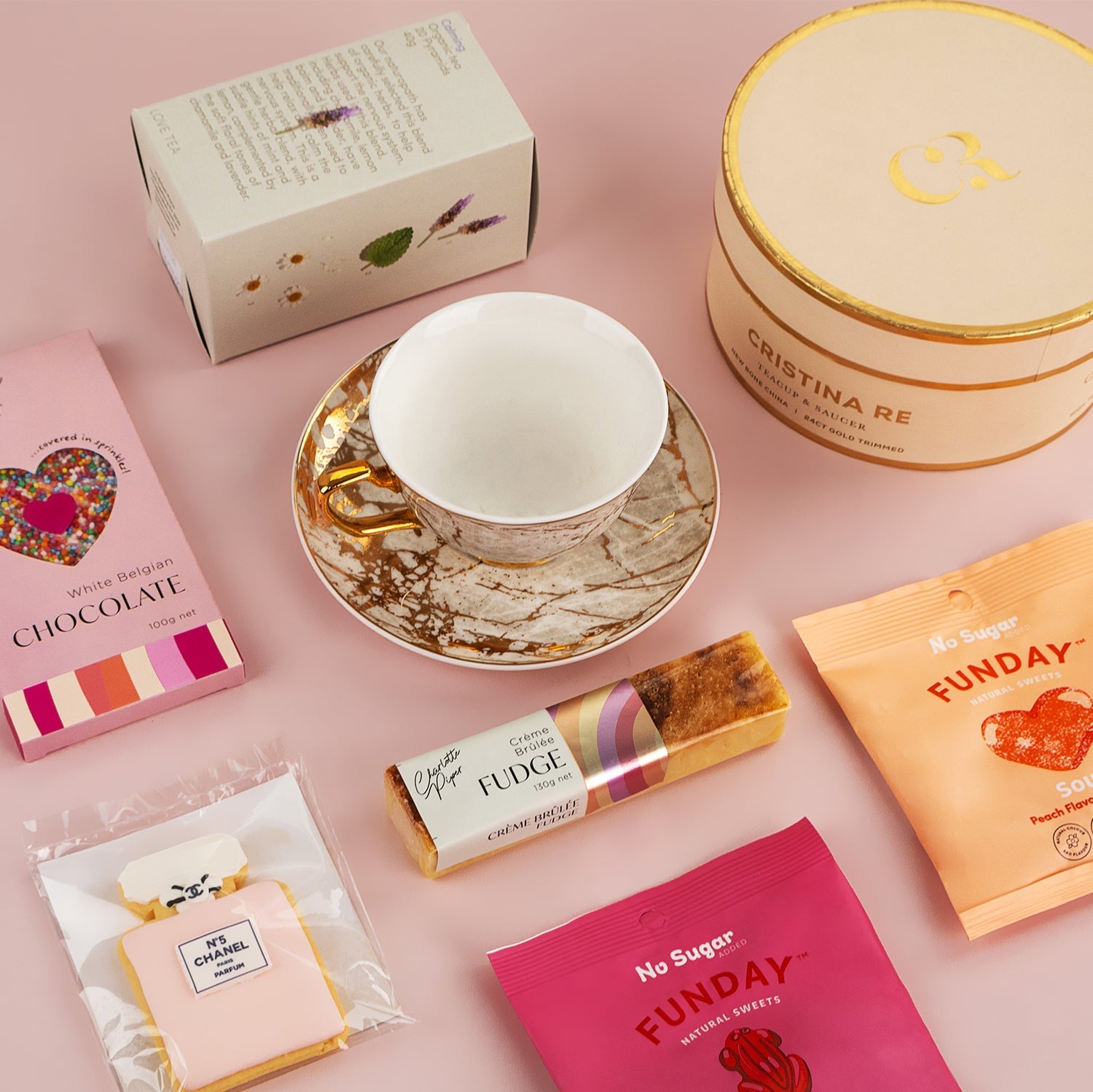 Elegant hamper featuring a marbled teacup and saucer, gourmet fudge, chocolate bar, floral tea box, and round gift box on.