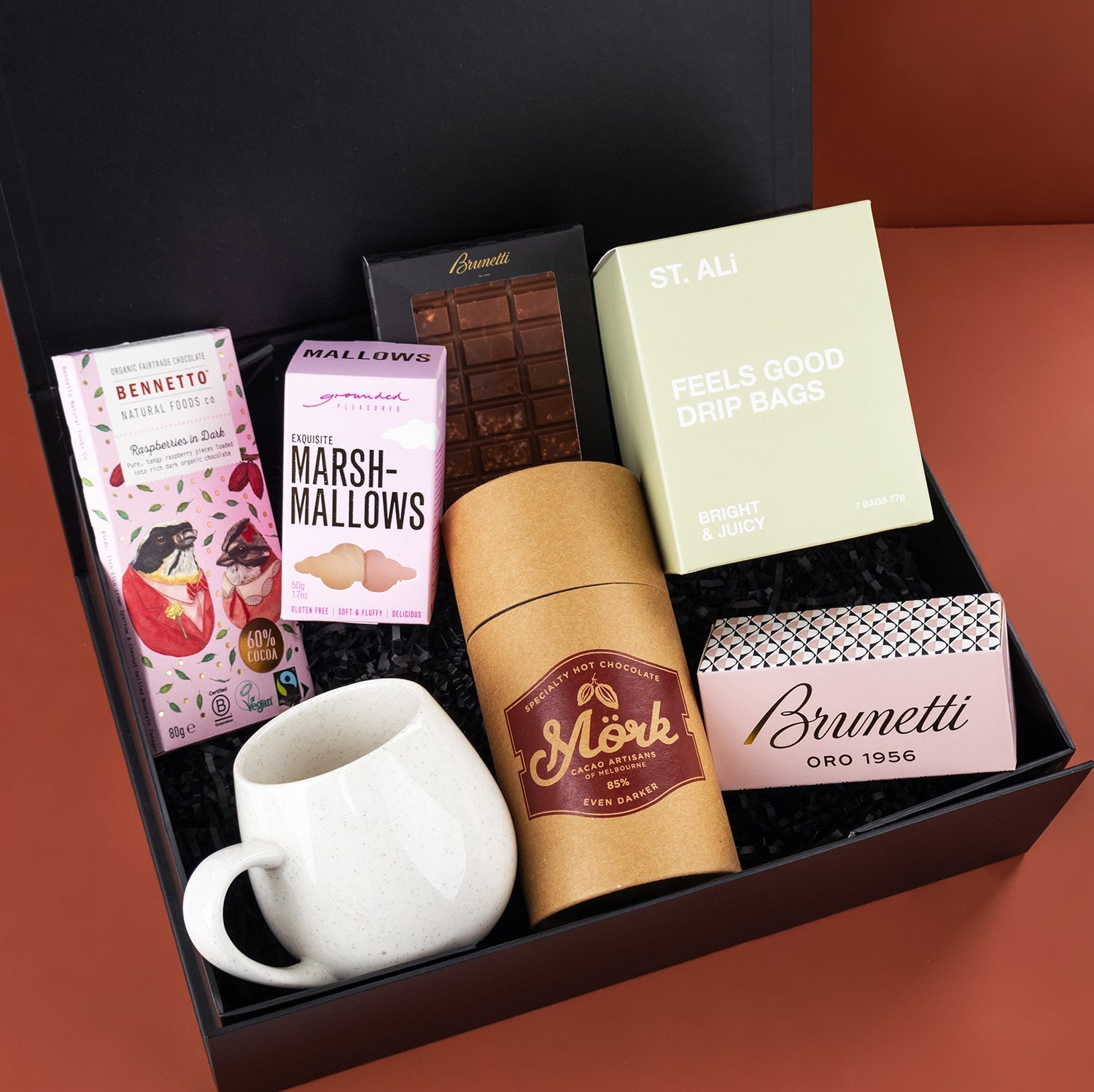 Black gift box with white ceramic mug, Monk coffee bag, Brunetti sweet biscuit box, marshmallows, chocolate bar, and green.