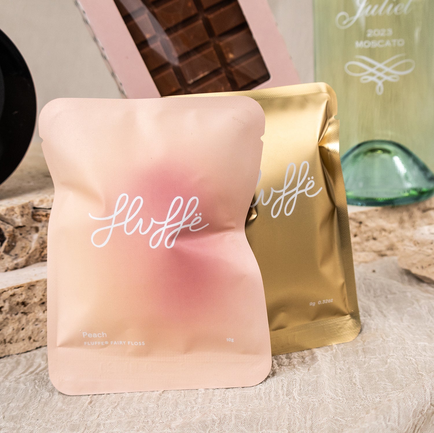 Two soft matte pouches in pink and gold with white "Fluffe" cursive logo on textured surface.