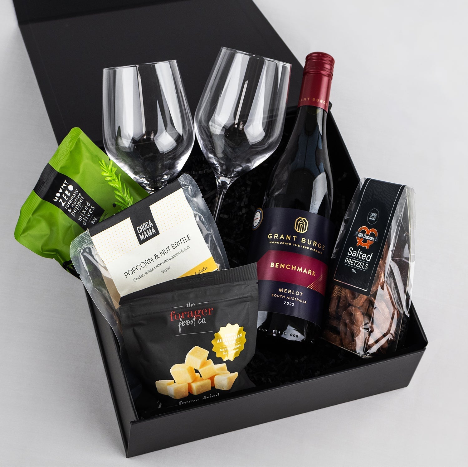 Black gift box with a bottle of Merlot, two wine glasses, cheese cubes, popcorn, and smoked nuts.