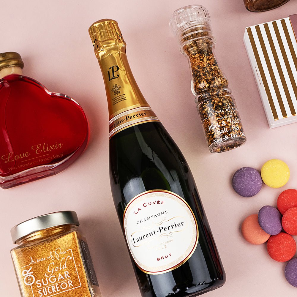 Laurent-Perrier La Cuvée champagne bottle with gourmet honey, spice grinder, colorful macarons, and red heart-shaped box on.