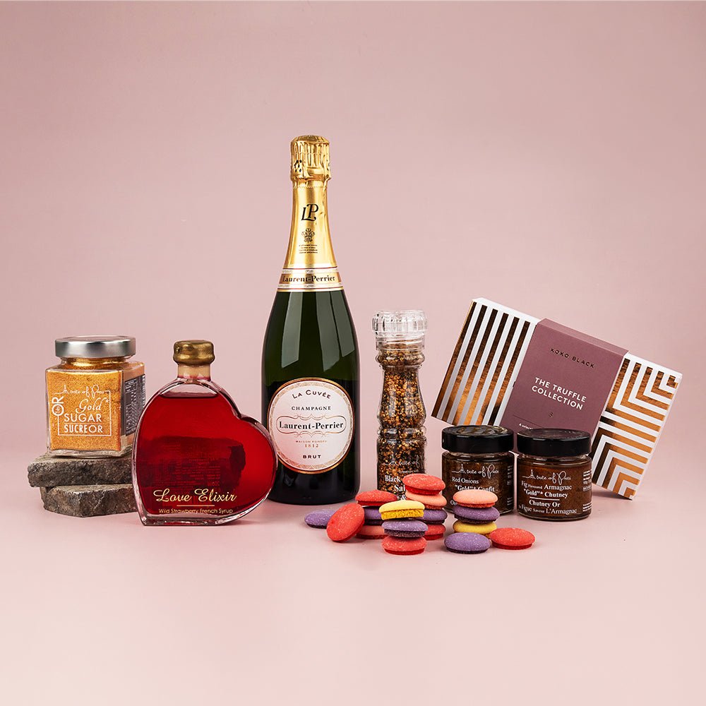 Gourmet hamper featuring sparkling wine, jar of mustard, bottle of liqueur, pepper grinder, two jars of preserves, colorful.